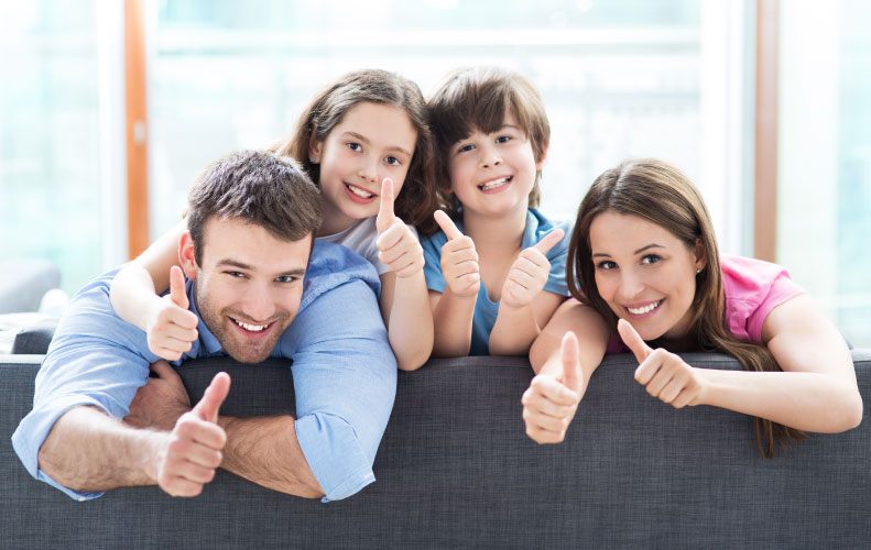 family on couch giving thumbs up for family dental care