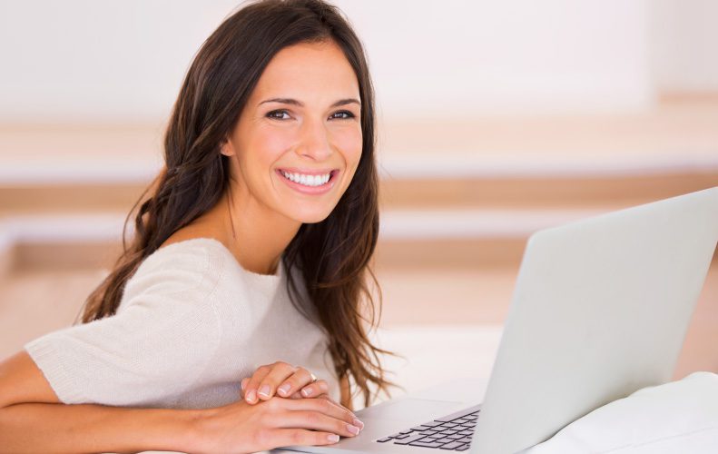 brunette woman with healthy gums at laptop smiling