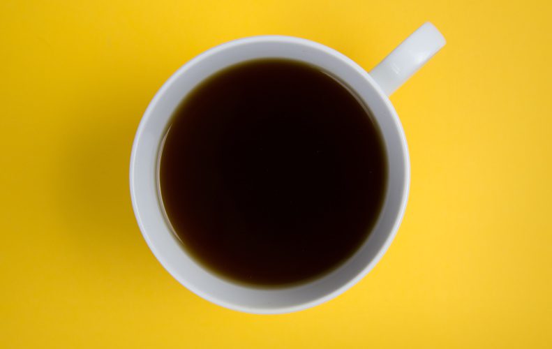 Aerial view of a white mug filled with brown coffee on a yellow counter