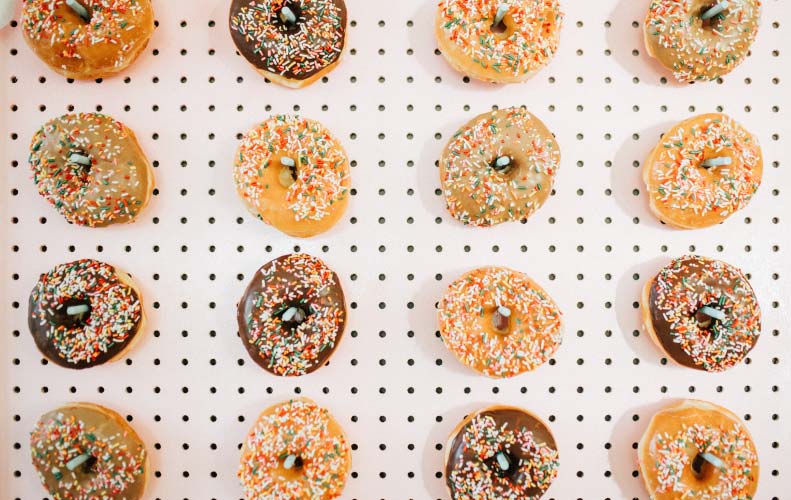 White pegboard filled with columns of chocolate and plain donuts covered with icing and sprinkles