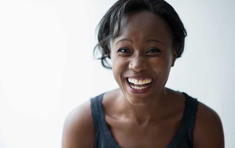 Closeup of a dark-haired woman wearing a gray tank top as she smiles brightly